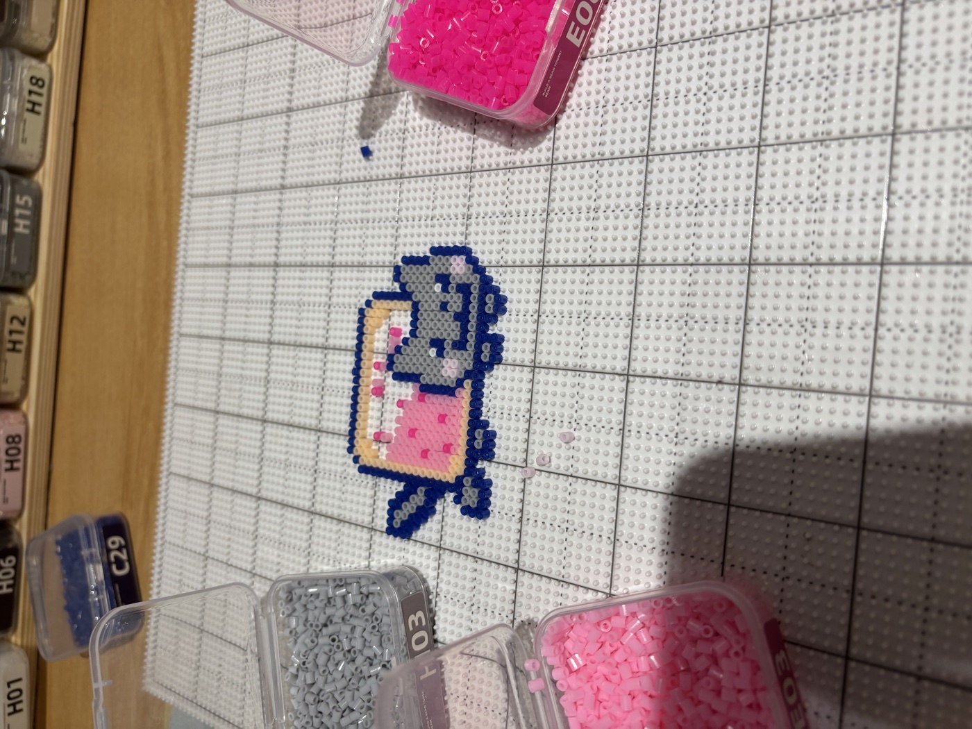 A fuse-bead cat I made on a pegboard, surrounded by tubs of pink, grey and blue beads